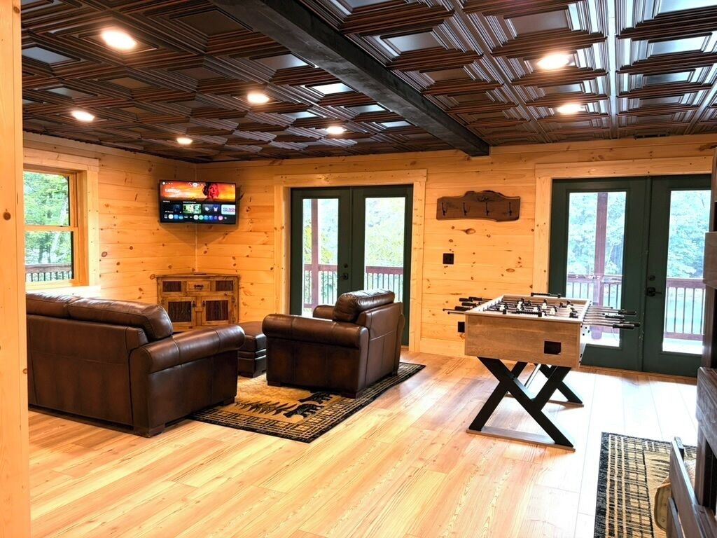 A cozy room with a wooden ceiling, a foosball table, leather sofas, and a television.