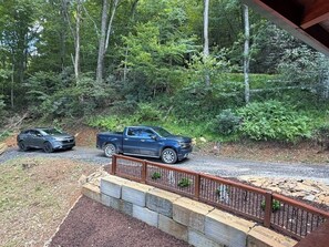 A driveway with a blue pickup truck parked on the side, surrounded by a stone retaining wall and a metal fence. - Log Cabin on the Lake with Private Dock-Hot Tub-Fireplace-Arcade-Close to town! (West Jefferson)