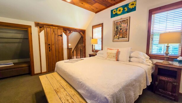 Una camera da letto con un letto, una panca di legno, un comodino, una lampada, un quadro e una finestra con persiane.