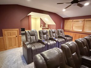 Ein Heimkinozimmer mit Ledersessel, Deckenventilator und Holztür.