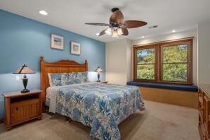 Une chambre à coucher comprenant un lit, deux tables de chevet, un ventilateur de plafond et une fenêtre avec des stores.