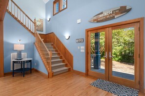 A staircase leading to a second floor, a round table with a lamp, a wall-mounted sign, and a glass door leading outside. - Beach ParTee Time: Soundfront, Private Pool, Hot Tub, Community Amenities (Corolla)
