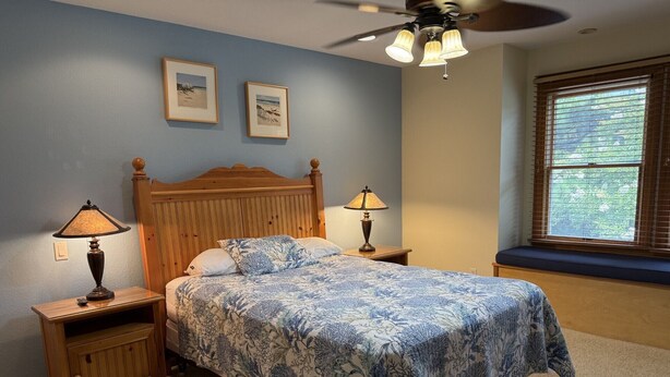 A bedroom with a wooden bed, two bedside lamps, a ceiling fan, and a window with blinds. - Beach ParTee Time: Soundfront, Private Pool, Hot Tub, Community Amenities (Corolla)
