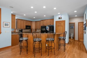 Une cuisine moderne avec des meubles en bois, un îlot central doté de tabourets de bar et des appareils électroménagers intégrés.