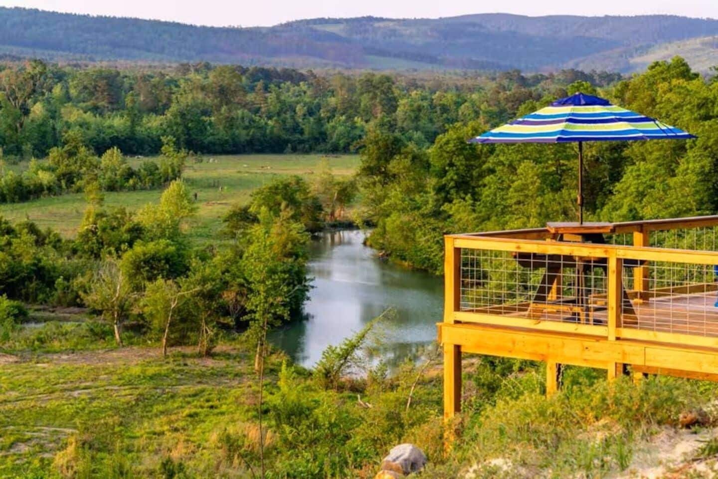 Vista al río con un muelle de madera y un paraguas a rayas.