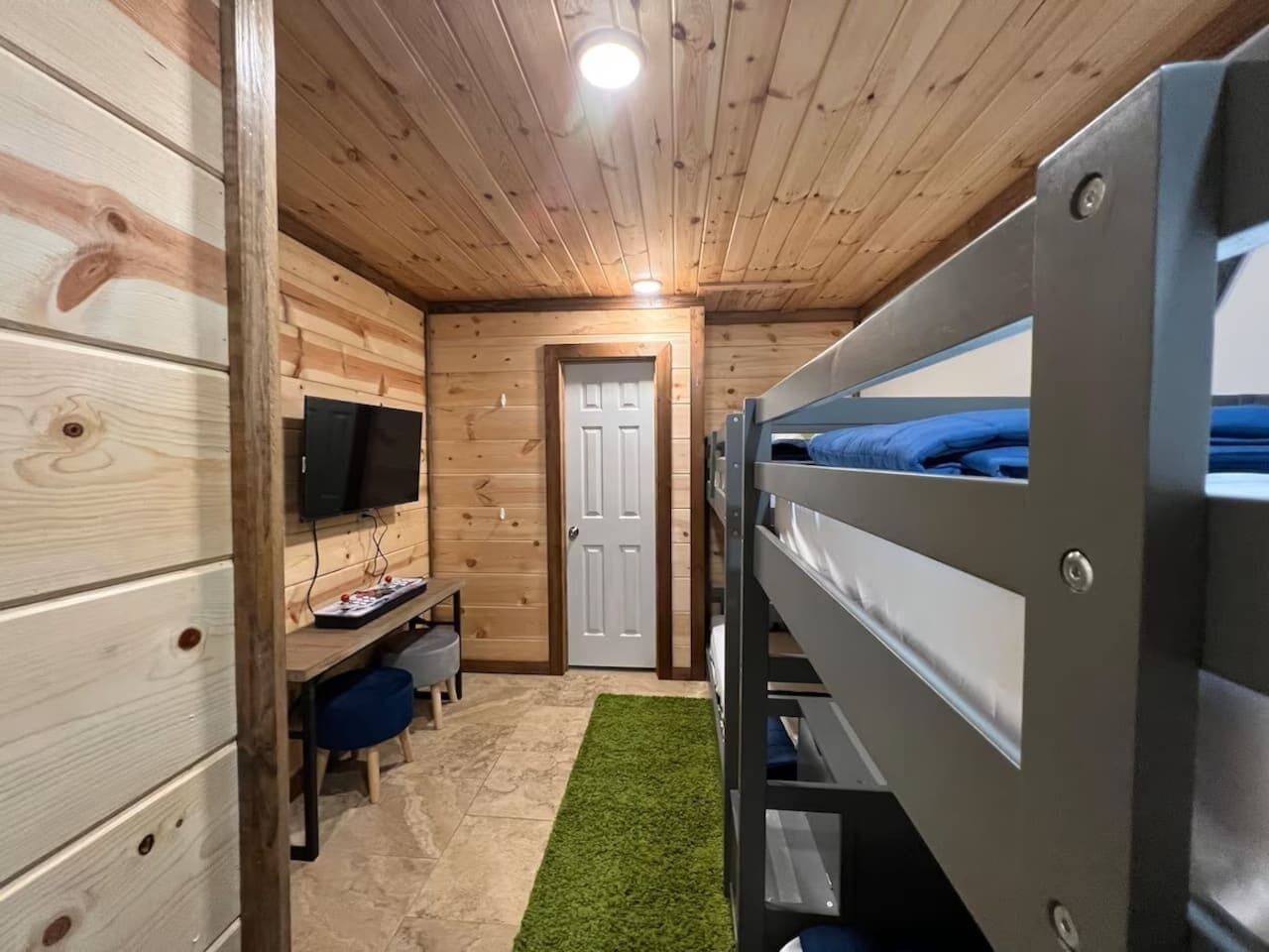 A room with bunk beds, a desk with a computer, a television, and a door.
