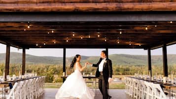 A wedding ceremony in a covered outdoor area with tables set for guests, surrounded by natural scenery.