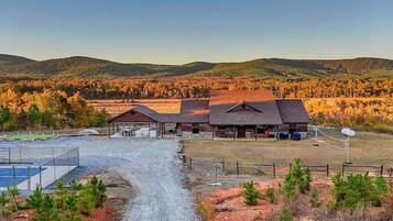 A rural property with a large barn, a covered outdoor seating area, and a gravel driveway leading to a fenced sports court.