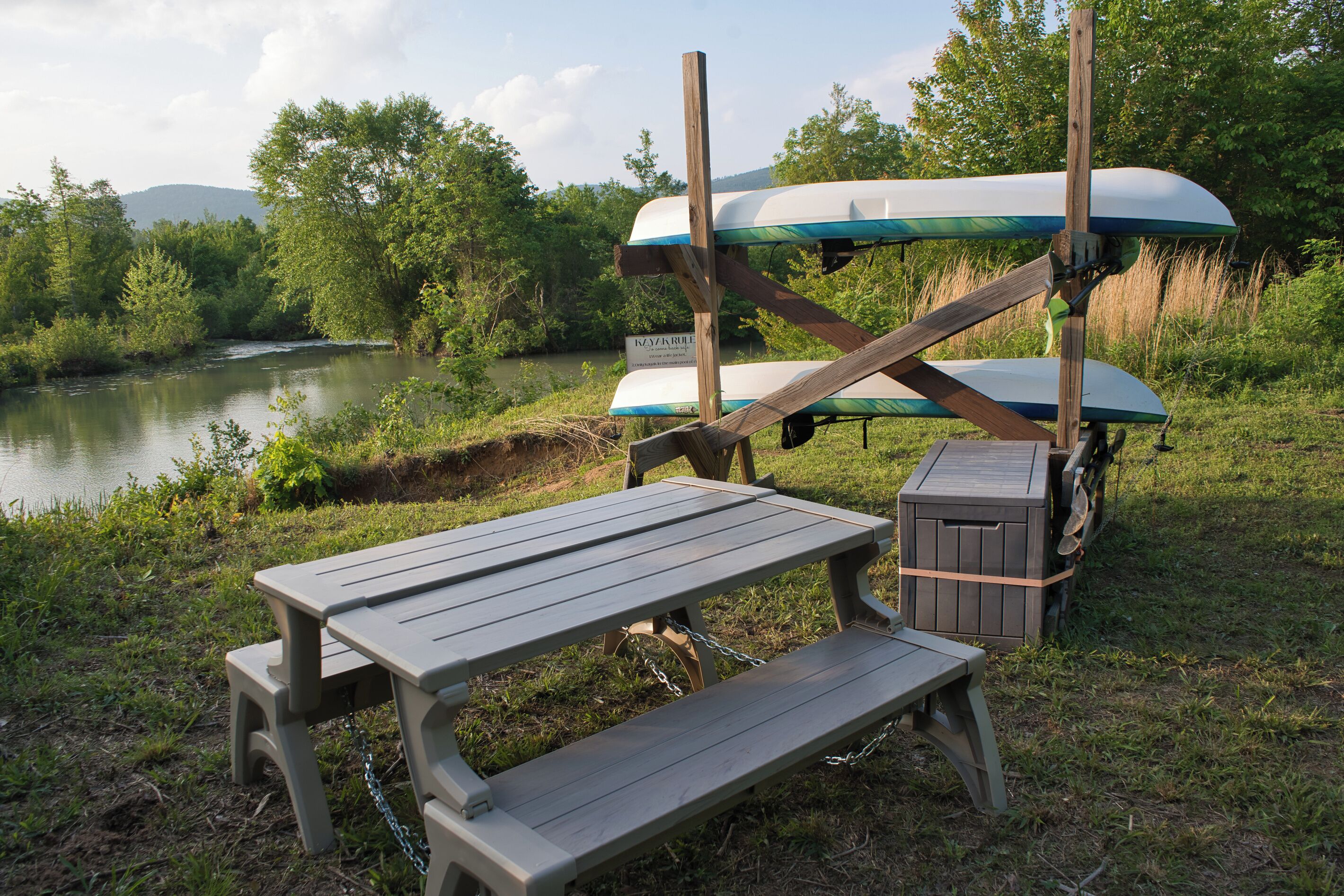 Un montaje para picnic con mesa y bancos, kayaks y un letrero que indica servicio de alquiler de kayaks.