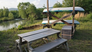 Un montaje para picnic con mesa y bancos, kayaks y un letrero que indica servicio de alquiler de kayaks.