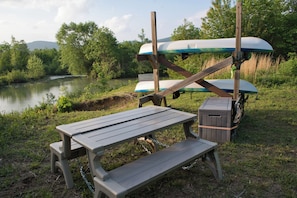 Picnicbord med bænke, kajakker og et skilt, der angiver en kajakudlejningsservice.