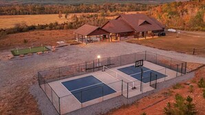 A property with a covered outdoor seating area, a tennis court, and a building with a red roof. - River Cabin with Pickleball and Kayaks (Smithville)