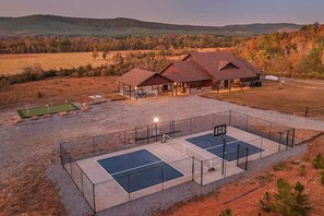 Ein Anwesen mit überdachter Außenbestuhlung, einem Tennisplatz und einem Gebäude mit rotem Dach.