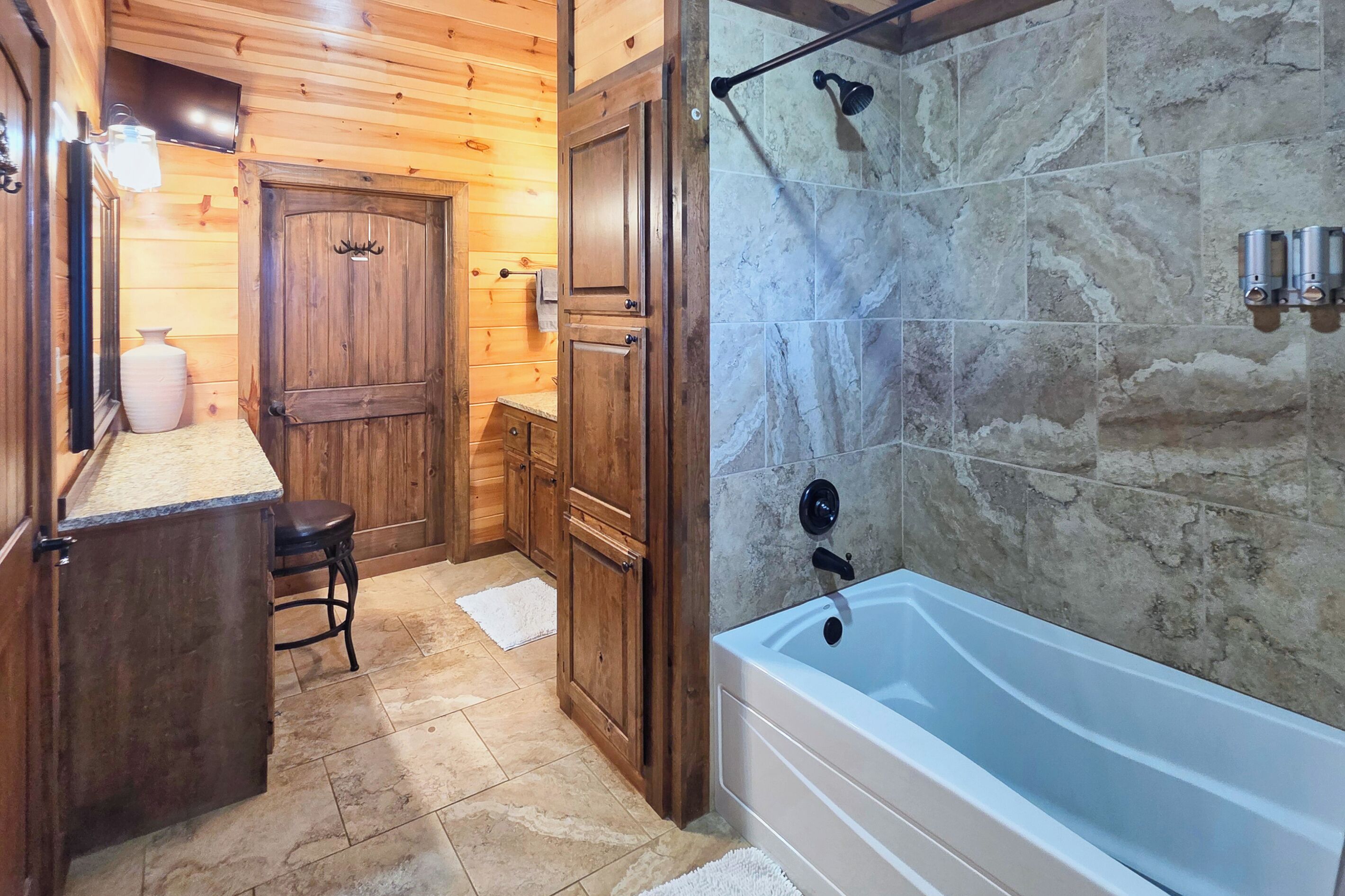 A wooden interior with a bathtub, a door with antlers, and a stone wall.
