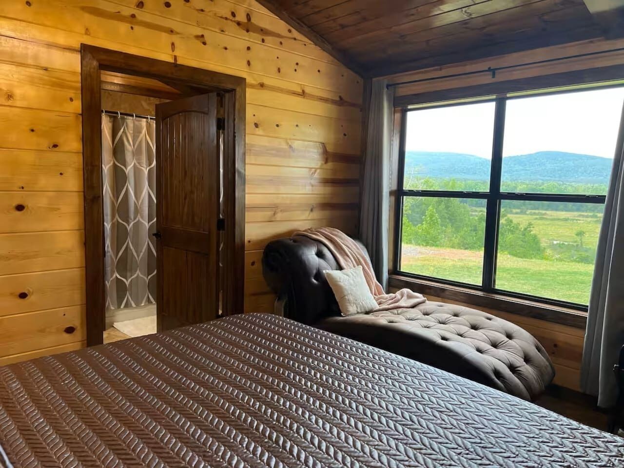 A bedroom with a bed, a window with a view of the outdoors, and a wooden door.