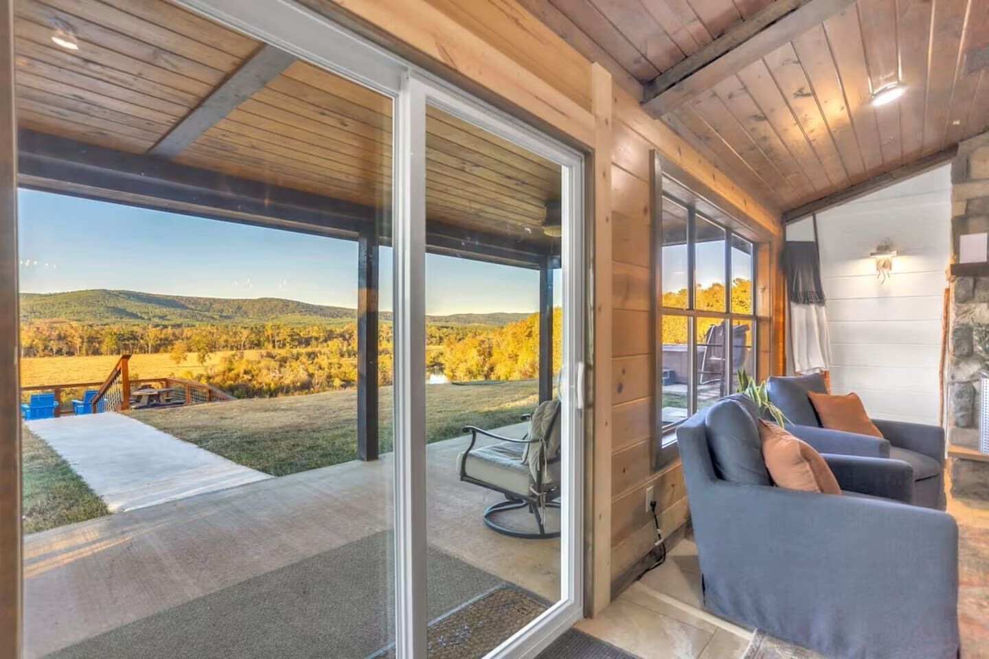 A modern interior with a large sliding glass door leading to an outdoor deck, a seating area with a sofa and armchairs, and a stone fireplace.