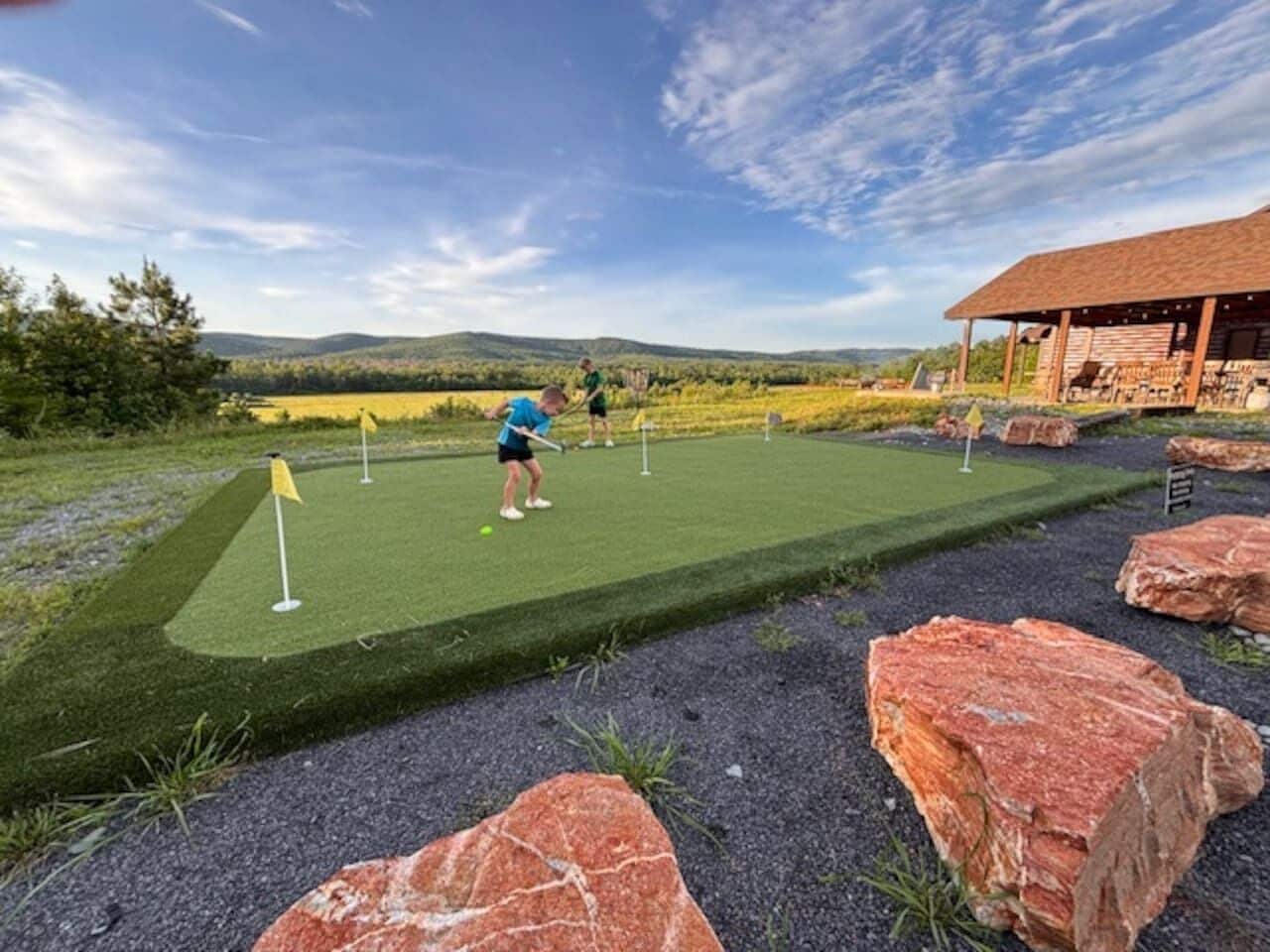 Un parcours de minigolf offrant une vue dégagée sur le paysage, un bâtiment doté d’un toit en pente et une personne qui joue.