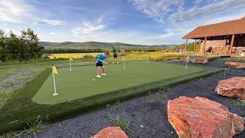 Un parcours de minigolf offrant une vue dégagée sur le paysage, un bâtiment doté d’un toit en pente et une personne qui joue.