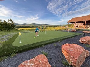 Un parcours de minigolf offrant une vue dégagée sur le paysage, un bâtiment doté d’un toit en pente et une personne qui joue.