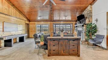 A spacious room with a wooden ceiling, a large window, a fireplace, and a seating area with a sofa and a dining table.
