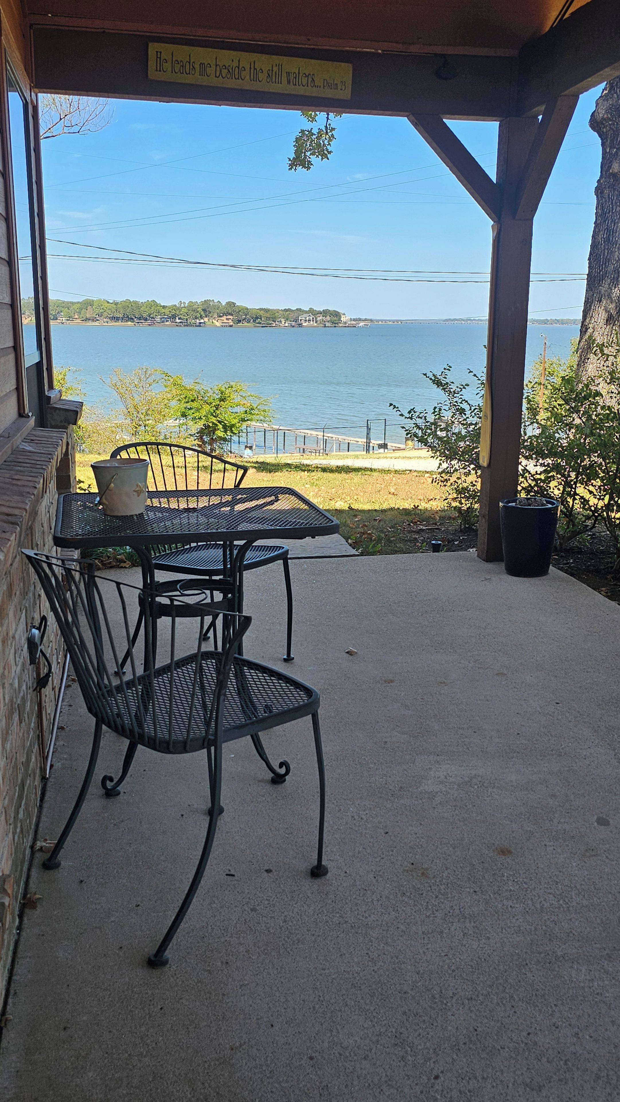 A covered patio with a table and chairs, overlooking a body of water and a distant shoreline.