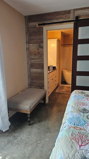 A bedroom with a bed, a bench, a bathroom with a bathtub, and a wooden wall.
