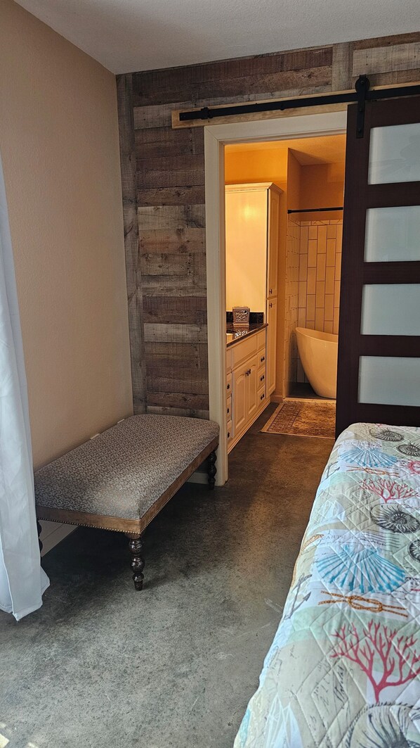 A bedroom with a bed, a bench, a bathroom with a bathtub, and a wooden wall. - Soaring Elevated Vast Lake Views from the Coolest Vantage Point and Park (Tool)