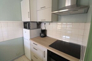 Eine kleine Küche mit weißen Schränken, einer eingebauten Mikrowelle, einer Kaffeemaschine und einer schwarzen Induktionskochplatte.