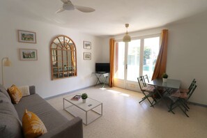 Ein Wohnzimmer mit Sofa, Couchtisch, Fernseher und einem Essbereich mit Stühlen und Tisch.