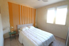 Ein Schlafzimmer mit einem Bett, zwei Nachttischen, einem Deckenventilator und einem Fenster.