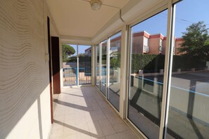 Ein Korridor mit großen Glasüren, die zu einem Außenbereich führen, einem Deckenventilator und einem gefliesten Boden.