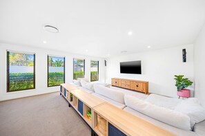 A modern living room with a sofa, television, and large windows with a view. - The Palms at Lake Cathie (Lake Cathie)