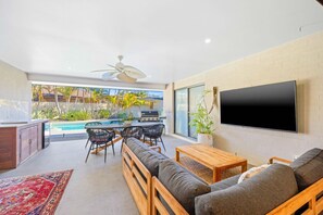 Ein modernes Wohnzimmer mit Fernseher, Sofa und Essbereich mit Blick auf einen Pool.