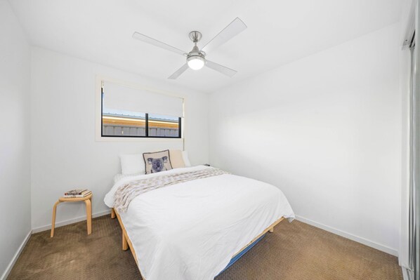 A bedroom with a bed, a small bedside table, a ceiling fan, and a window with a view.