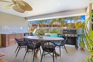 A patio with a round table, four chairs, a grill, and a pool in the background. - The Palms at Lake Cathie (Lake Cathie)