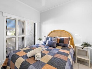 Un lit bien fait, avec une couvre-lit à carreaux, une tête de lit en bois et une table de chevet sur laquelle se trouvent une lampe et une plante.