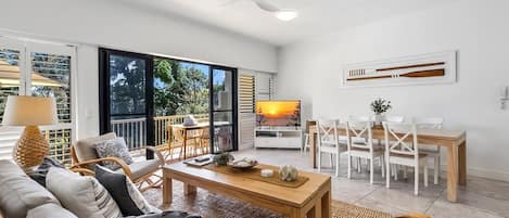 A spacious living area with a ceiling fan, a dining table with chairs, and a large window providing a view of the outdoors.