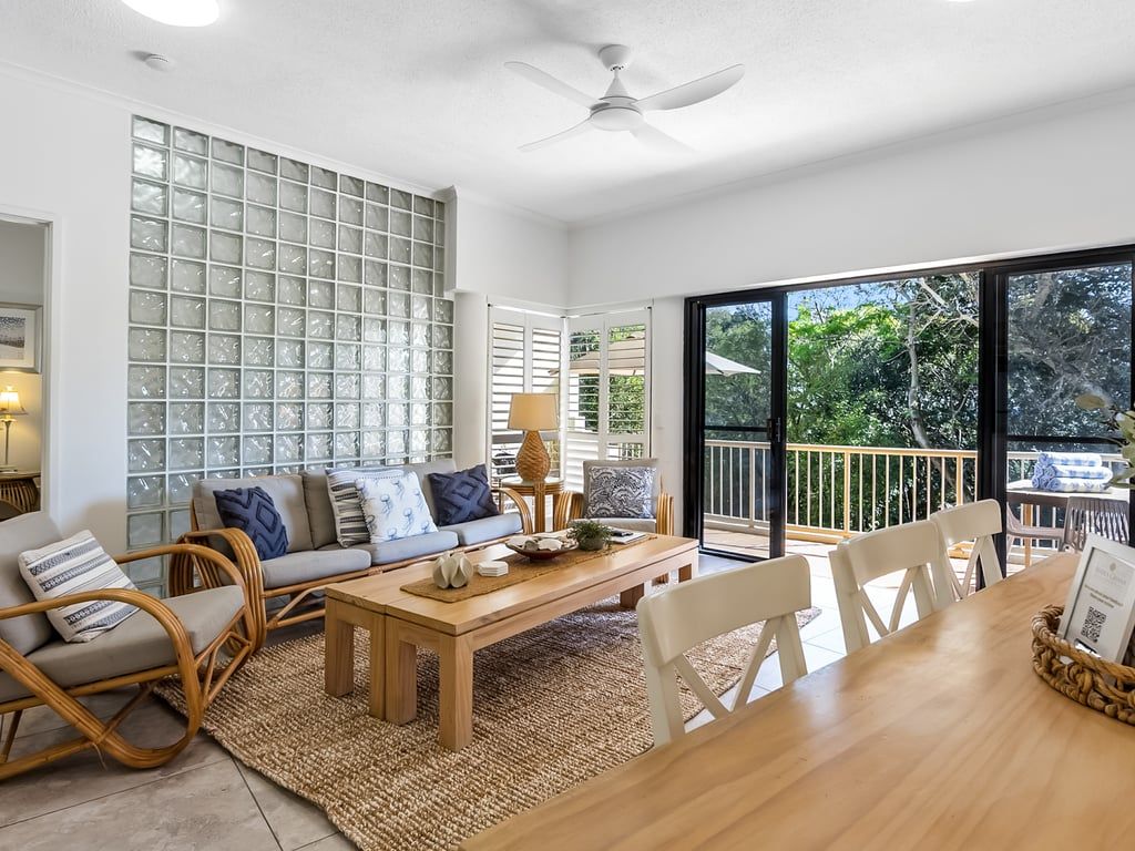Un salon moderne comprenant un canapé, une table basse et des fauteuils, un grand mur de verre et un balcon aménagé avec du mobilier d’extérieur.