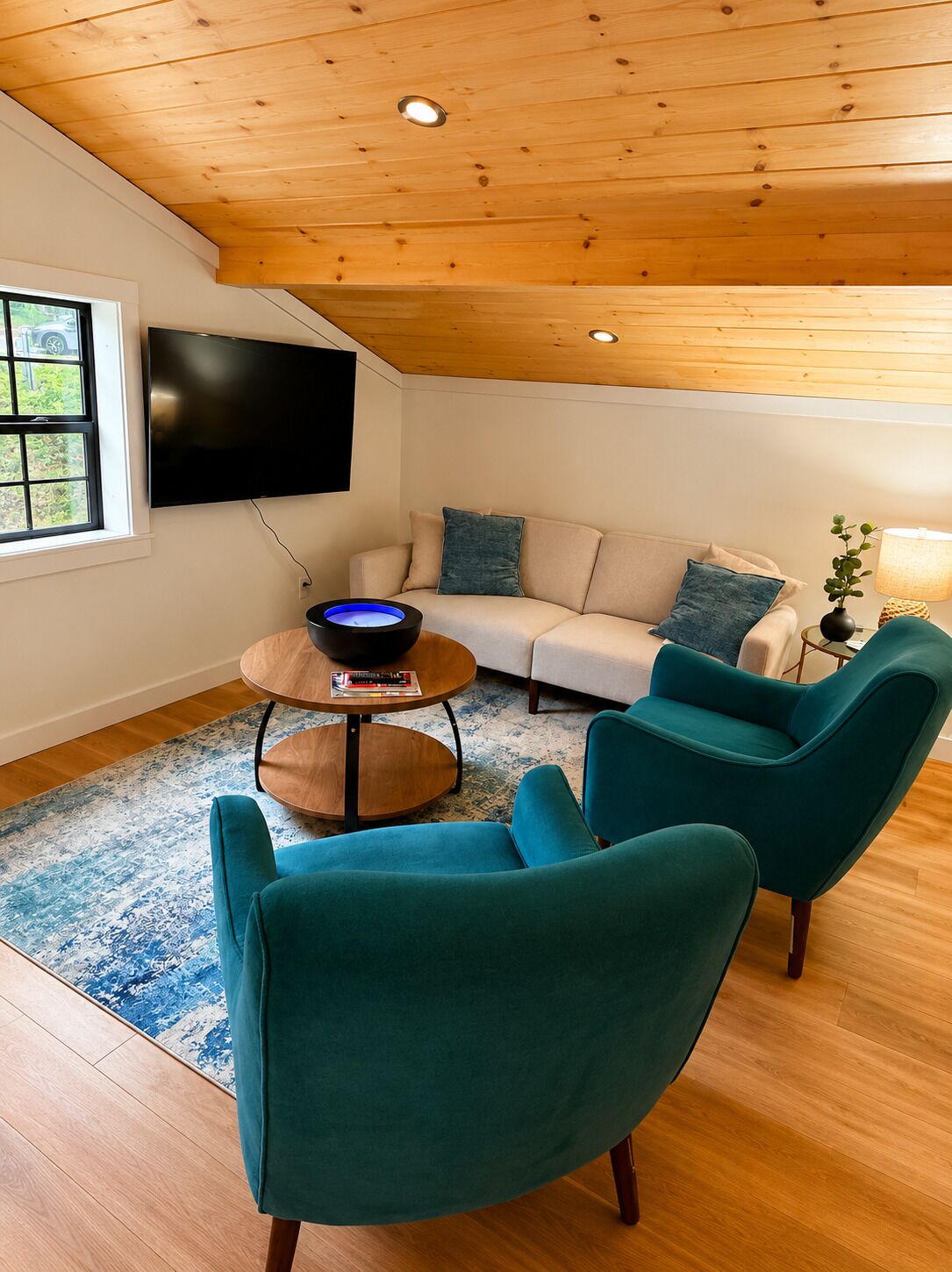 A cozy living room with a sofa, two armchairs, a coffee table, and a flat-screen TV mounted on the wall.