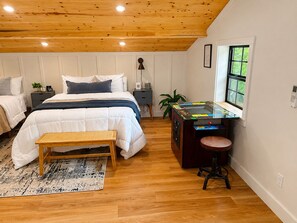 A bedroom with a bed, bedside tables, a desk with a computer, a window, and a plant.