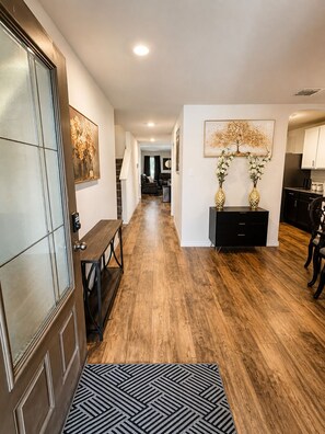 A hallway with wooden flooring, a bench, a door with glass panels, and a black and white rug. - Pool Retreat - 5BR - Sleeps 16+ - Lackland AFB (San Antonio)