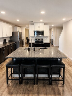 A modern kitchen with a central island, stainless steel appliances, and a dark wood floor. - Pool Retreat - 5BR - Sleeps 16+ - Lackland AFB (San Antonio)