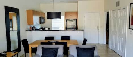 A modern kitchen with a dining area, featuring a central island, chairs, and a television.