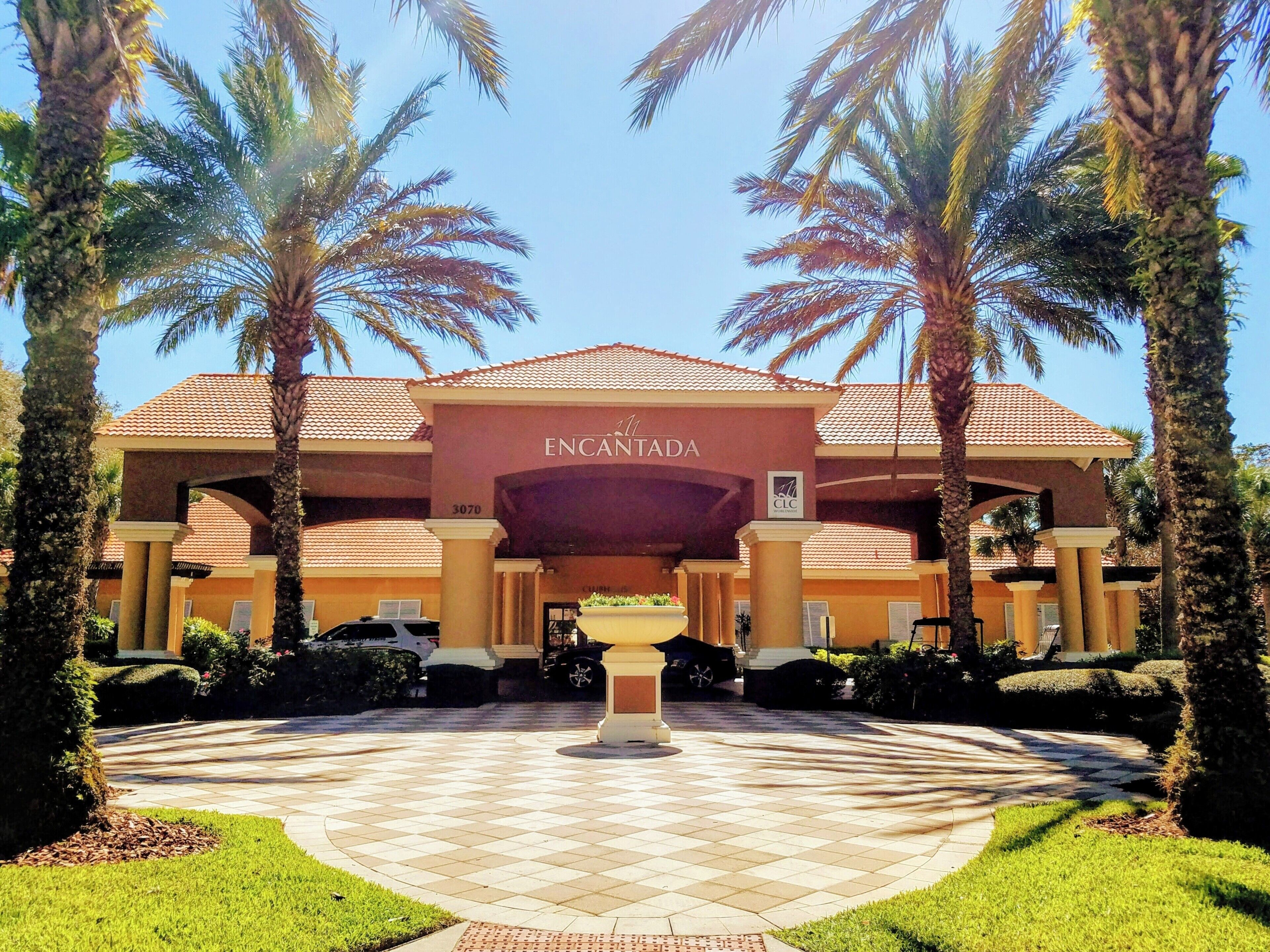 A hotel entrance with a tiled driveway, palm trees, and a sign reading 'ENCANTADA'.