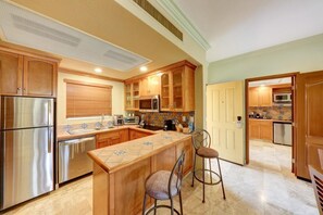 Cucina con mobili in legno, elettrodomestici in acciaio inossidabile, zoccolo schienale piastrellato e angolo bar con sgabelli.