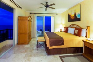 Una camera d'hotel con un letto, una scrivania, una sedia, una ventola a soffitto e vista sull'oceano.
