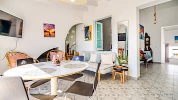 Una sala moderna con una mesa redonda de comedor, un sofá y una mesa de centro. Hay un televisor montado en la pared, y el piso está cubierto de baldosas.