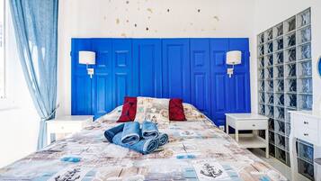 Un dormitorio con cabecera azul, cama con colcha de temática náutica, dos lámparas de noche y una mesita de noche blanca.