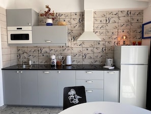 Una cocina compacta con armarios grises, encimera negra y salpicadero de azulejos con diseño floral.
