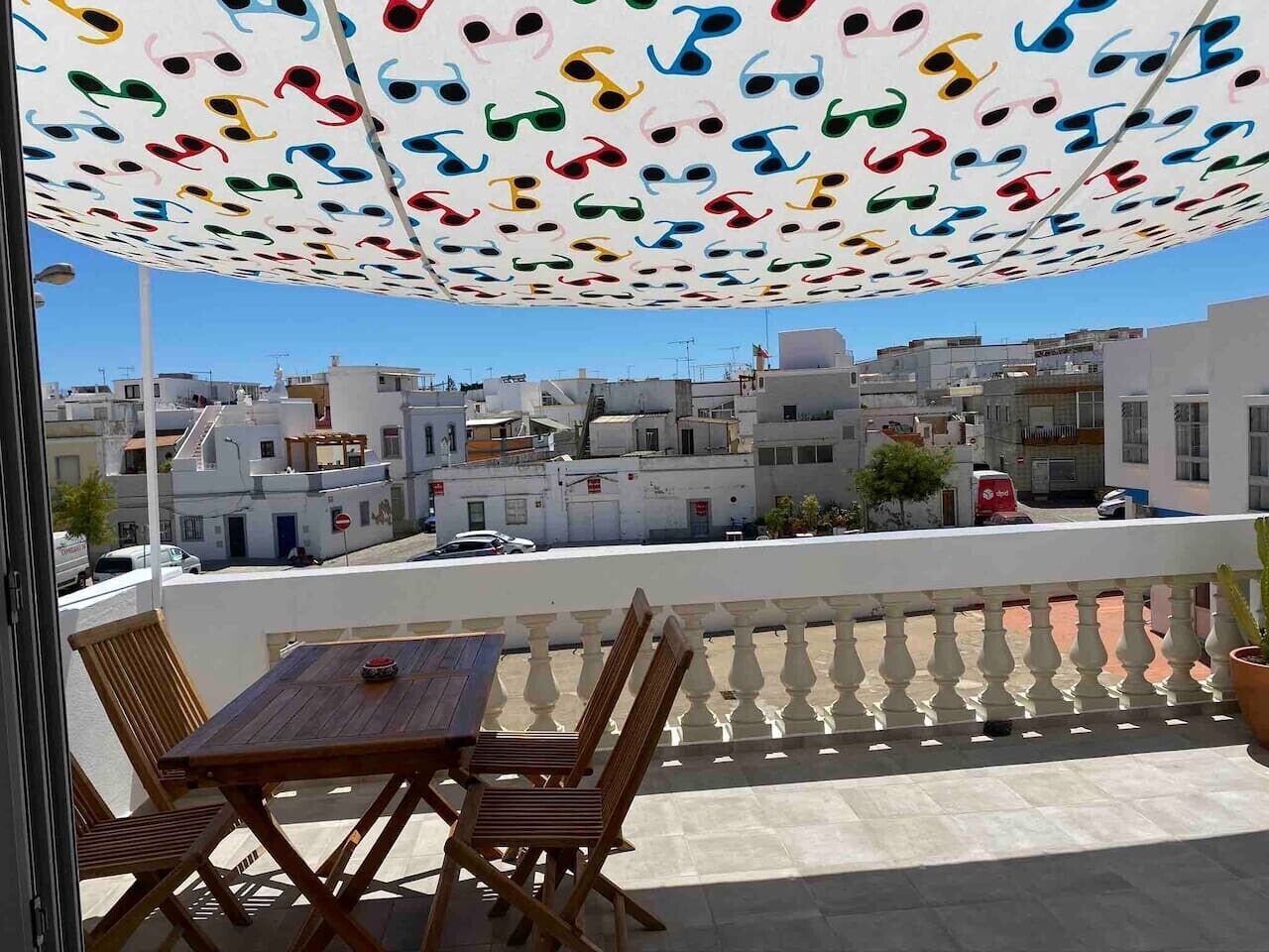 Un balcone con tavolo e sedie in legno, un ombrellone decorato e vista sui palazzi.